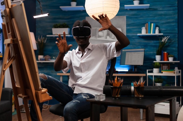 Afroamerikanischer Künstler auf der Suche nach Inspiration im Online-Universum mit Virtual-Reality-Brille im heimischen Kunststudio. Junger Zeichenstudent auf der Suche nach neuen künstlerischen Techniken bei Metaverse.