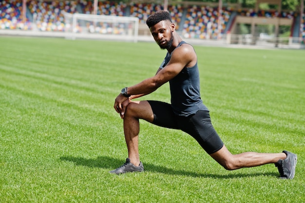 Afroamerikanischer männlicher Athlet in Sportkleidung, der Dehnübungen im Stadion macht