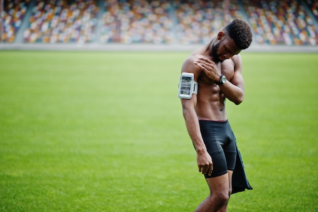 Afroamerikanischer männlicher Athlet sexy Sport mit nacktem Oberkörper Mann mit laufendem Sportarmgehäuse für Handy posierte auf grünem Gras des Fußballstadions