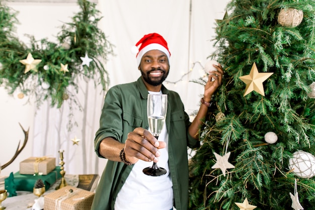 Afroamerikanischer Mann, der Champagner nahe Weihnachtsbaum hält