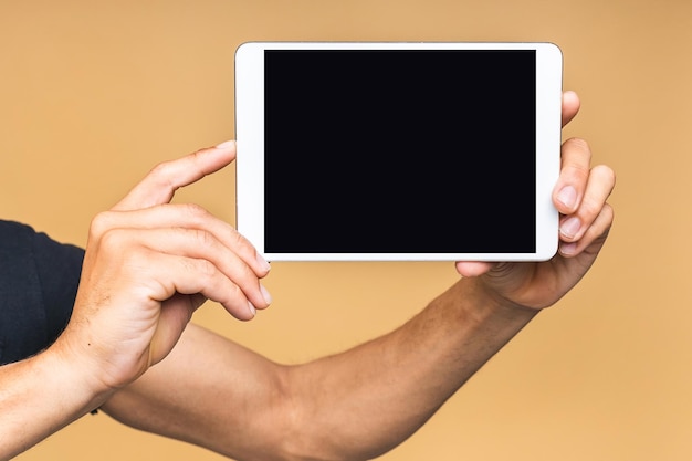 Afroamerikanischer Mann, der eine Tablette auf beigem Hintergrund isoliert hält Copyspace Closeup-Konzept Hand mit Tablet-Computer