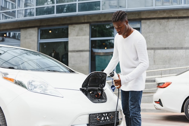 Afroamerikanischer Mann, der sein Elektroauto auflädt.