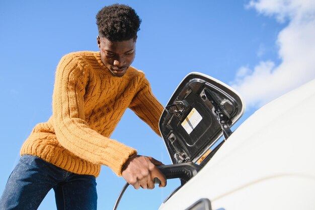 Afroamerikanischer Mann, der sein Elektroauto auflädt.