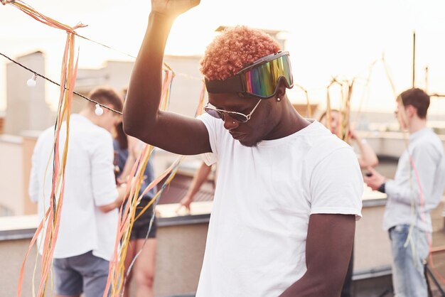 Afroamerikanischer Mann lächelt und tanzt Gruppe junger Leute in lässiger Kleidung feiern tagsüber gemeinsam auf dem Dach