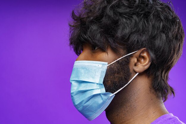 Afroamerikanischer Mann mit medizinischer Gesichtsmaske vor violettem Hintergrund