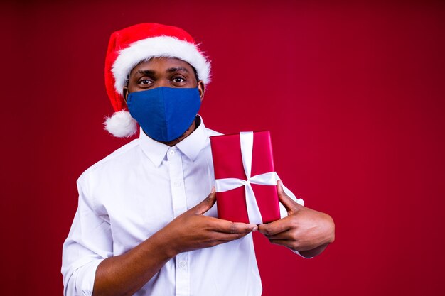 Afroamerikanischer Mann mit Weihnachtsmütze und Maske im roten Studiohintergrund