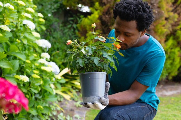 Afroamerikanischer Mann trägt Gartenhandschuhe und riecht Blumen, während er im Garten arbeitet