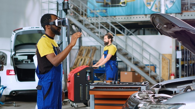 Afroamerikanischer Mechaniker im Autoservice simuliert mit einer Virtual-Reality-Brille die Reaktion eines Autos auf die Straßenverhältnisse nach der Reparatur. Mechaniker trägt High-Tech-VR-Headset, um den Fahrzeugmotor zu testen