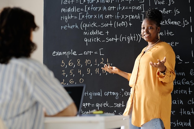 Afroamerikanischer Nachhilfelehrer steht neben der Tafel und erklärt dem Schüler im Unterricht den Stoff