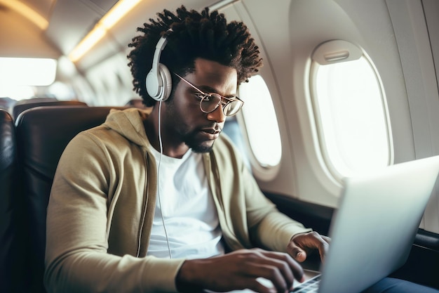 Afroamerikanischer Passagier mit Laptop und Kopfhörern im Flugzeug