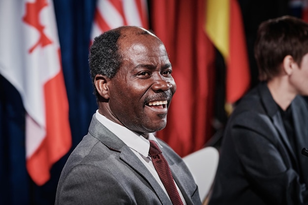 Afroamerikanischer Politiker im Anzug lacht, während er bei internationalen Treffen mit Kollegen sitzt