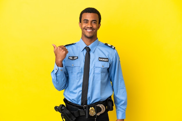 Afroamerikanischer Polizist über isoliertem gelbem Hintergrund, der auf die Seite zeigt, um ein Produkt zu präsentieren