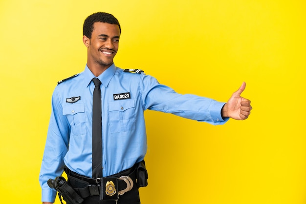 Afroamerikanischer Polizist über isoliertem gelbem Hintergrund, der eine Geste mit dem Daumen nach oben gibt