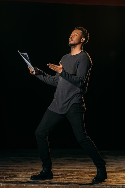 Afroamerikanischer Schauspieler hält Szenario und steht während der Probe im Theater auf der Bühne