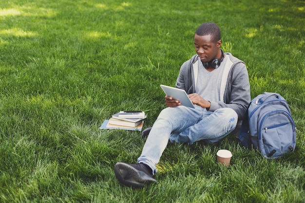 Afroamerikanischer Student mit Tablet im Freien. Gelegenheitsstudent, der E-Mails checkt und im Internet auf einem digitalen Gerät auf dem Universitätscampus surft. Technologie, soziale Medien, Bildungskonzept, Kopierraum