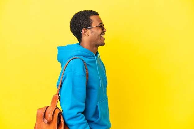 Afroamerikanischer Studentenmann über isoliertem gelbem Hintergrund, der in seitlicher Position lacht