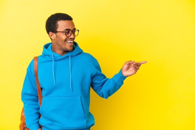 Afroamerikanischer Studentenmann über isoliertem gelbem Hintergrund, der mit dem Finger zur Seite zeigt und ein Produkt präsentiert