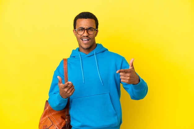 Afroamerikanischer Studentenmann über isoliertem gelbem Hintergrund, der nach vorne zeigt und lächelt