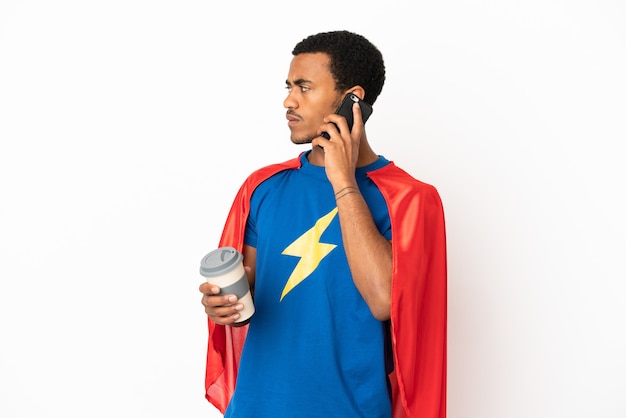 Afroamerikanischer Superheld-Mann über isoliertem weißem Hintergrund, der Kaffee zum Mitnehmen und ein Handy hält
