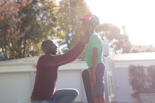 Afroamerikanischer Vater und Sohn lächeln und bereiten sich vor, bevor sie im sonnigen Garten Skateboard fahren. Familie verbringt Zeit zu Hause.