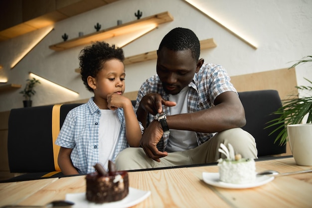 Afroamerikanischer Vater und Sohn überprüfen die Armbanduhr, während sie zusammen im Café sitzen