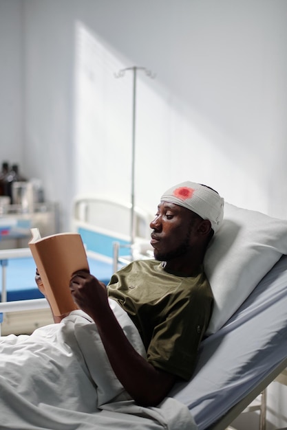 Afroamerikanischer verwundeter Soldat liegt auf dem Bett und liest ein Buch im Krankenhaus