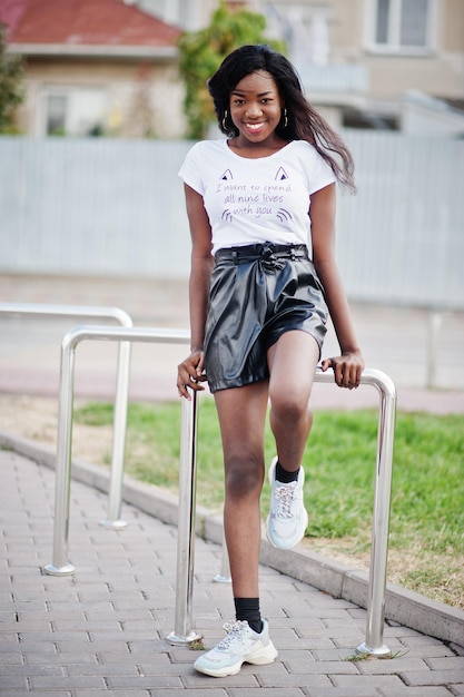 Afroamerikanisches, dunkelhäutiges, schlankes Modell, das in einer schwarzen Lederhose und einem weißen T-Shirt posiert