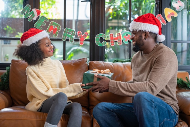 Afroamerikanisches Mädchen, das ihrem Vater oder Papa zuhause zu Hause bei Merry Christmas eine Geschenkbox gibt