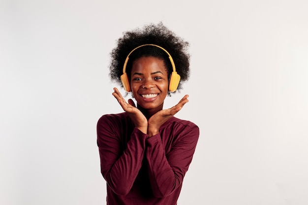 Afroamerikanisches Mädchen in braunem Pullover posiert beim Lächeln und Musikhören.