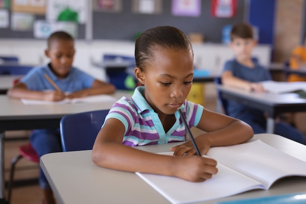 Afroamerikanisches Mädchen lernt, während sie in der Schule auf ihrem Schreibtisch sitzt