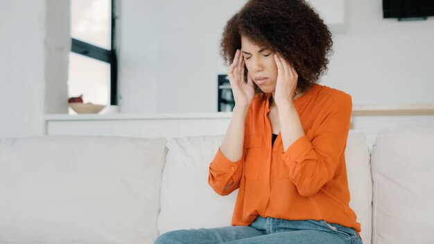 Afroamerikanisches Mädchen mit lockigem Haar, Frau sitzt zu Hause auf der Couch und berührt Massagen an den Schläfen