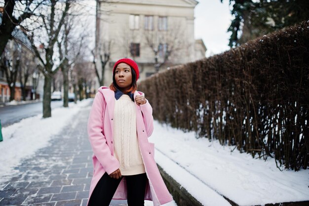 Afroamerikanisches Mädchen mit rotem Hut und rosa Mantel auf der Straße der Stadt am Wintertag