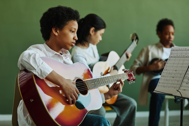 Afroamerikanisches Schulmädchen mit akustischer Gitarre, das Papier mit Musiknoten betrachtet, während es i spielt