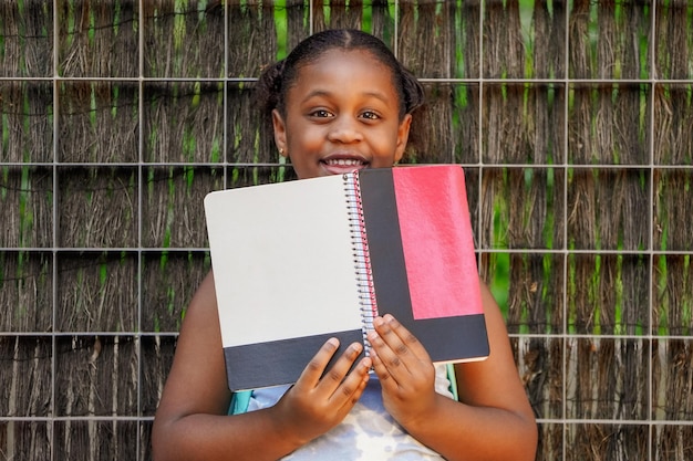 Afroamerikanisches Schulmädchen mit Rucksackkopfhörern und Notizbüchern am Schuleingang