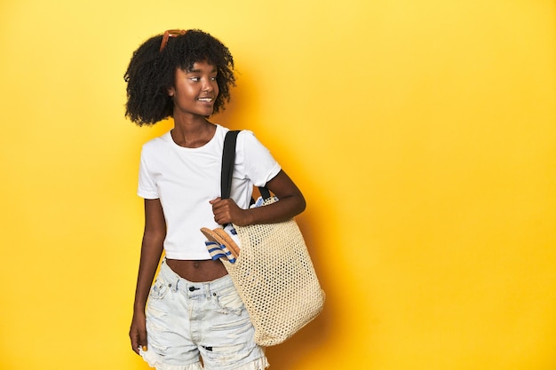 Afroamerikanisches Teenager-Mädchen bereit für den Strand mit Accessoires auf gelben Studio-Hintergrund