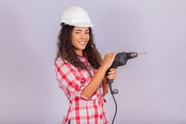 Afrofrau, die eine elektrische Bohrmaschine auf weißem Hintergrund hält.