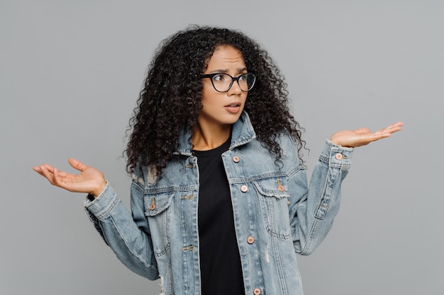 Afrofrau mit dem klaren Haar, hebt Hände in der Verwirrung an, schaut beiseite