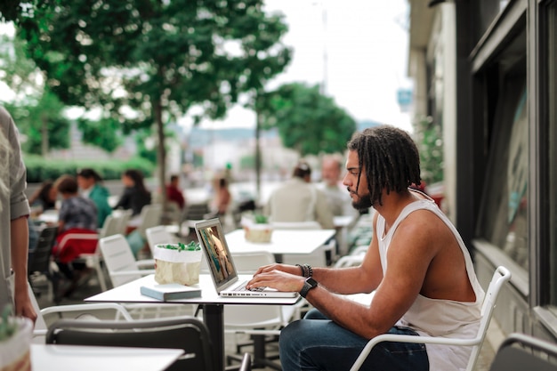 Afrokerl, der an einem Laptop auf der Terrasse eines Cafés arbeitet