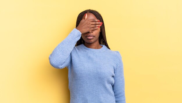 Afroschwarze hübsche Frau, die die Augen mit einer Hand bedeckt, sich verängstigt oder ängstlich fühlt, sich wundert oder blind auf eine Überraschung wartet