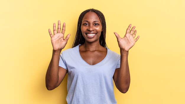 Afroschwarze hübsche Frau, die lächelt und freundlich aussieht und die Nummer zehn oder zehn zeigt, wobei die Hand nach unten zählt