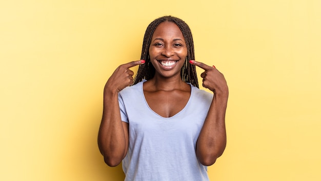 Afroschwarze hübsche Frau, die selbstbewusst auf ihr eigenes breites Lächeln lächelt, positive, entspannte, zufriedene Einstellung