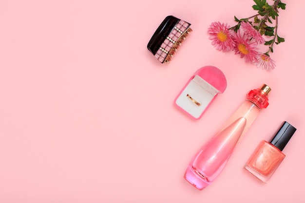 Agarre para el cabello, caja con aro dorado, flores, frasco de perfume y frasco con esmalte de uñas sobre fondo rosa. Cosmética y complementos para mujer. Vista superior con espacio de copia.