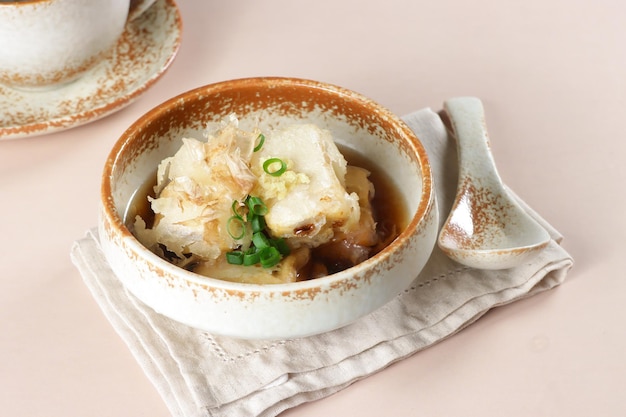 Agedashi é tofu frito servido em caldo quente de dashi e decorado com gengibre ralado e cebolinha picada.