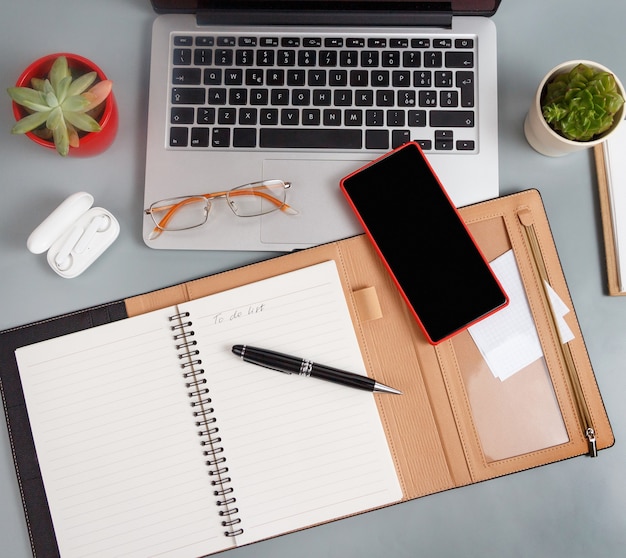 Agenda abierta con texto LISTA DE HACER cerca de una computadora portátil y dispositivos modernos en una vista superior de escritorio gris