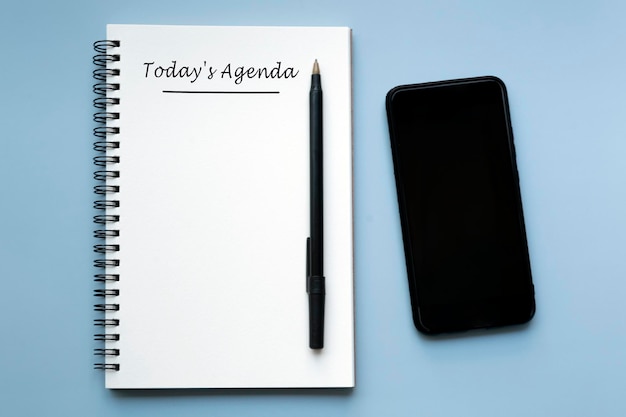 Foto agenda de hoje escrita num caderno com caneta e smartphone sobre fundo azul