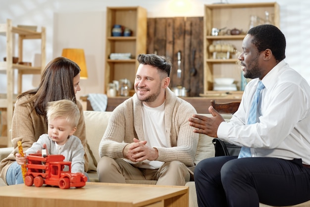 Agente afroamericano hablando con una pareja joven con un niño sobre hipotecas inmobiliarias