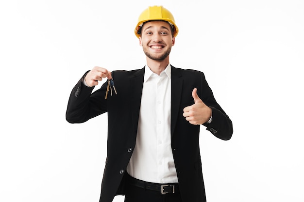 Foto agente de bienes raíces alegre joven en casco de seguridad amarillo que muestra felizmente el pulgar hacia arriba mientras