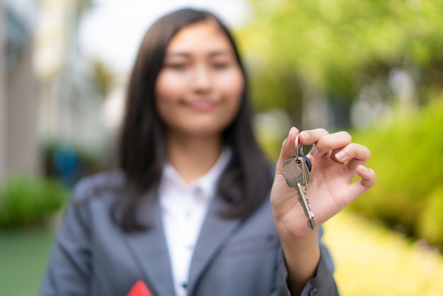 Agente de bienes raíces o mujer inmobiliaria sonriendo y sosteniendo un archivo rojo con la llave de la casa que muestra