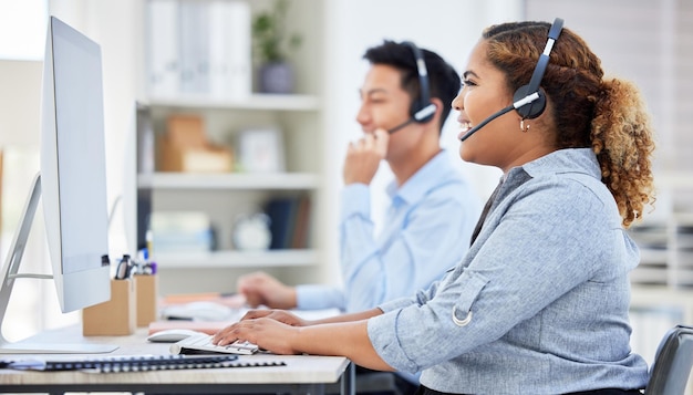 Agente de centro de llamadas feliz, confiado y sonriente, hablando con un auricular mientras trabaja en una computadora en una oficina Vendedora o consultora que opera una mesa de ayuda para atención al cliente y soporte de servicio