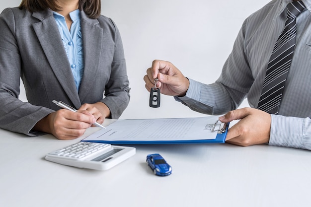 Agente de aluguel de carros que dá a chave de um carro novo para um cliente